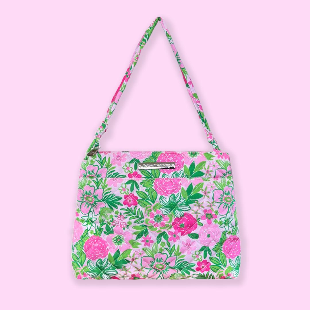 A quilted crossbody hipster bag with a pink and green floral pattern, featuring a shoulder strap, zipper closure, and multiple pockets.